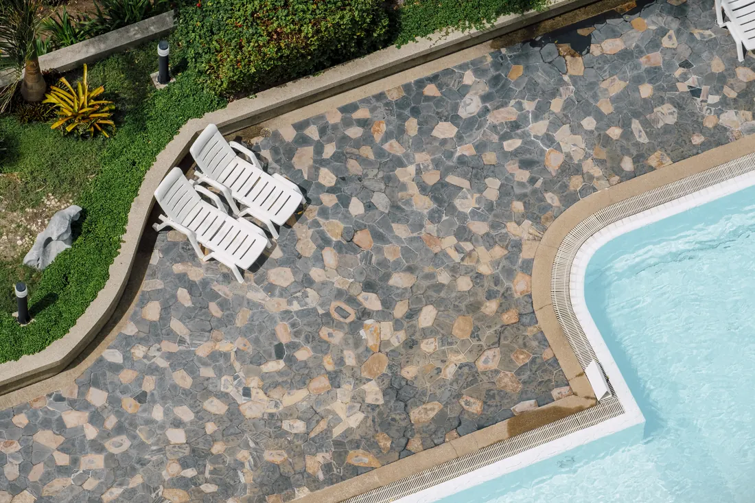 Aerial view of a pool deck with stone paver hardscape and lounge chairs